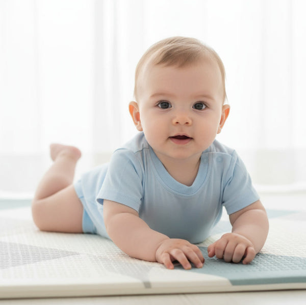 Baby in a light blue onesie lying on a white mat with a white curtain background