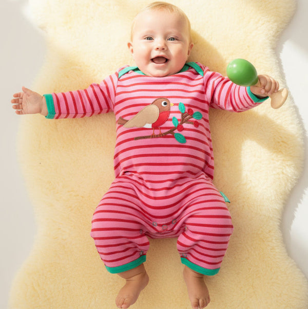 Baby in a pink striped outfit lying on a yellow cushion with a green ball.