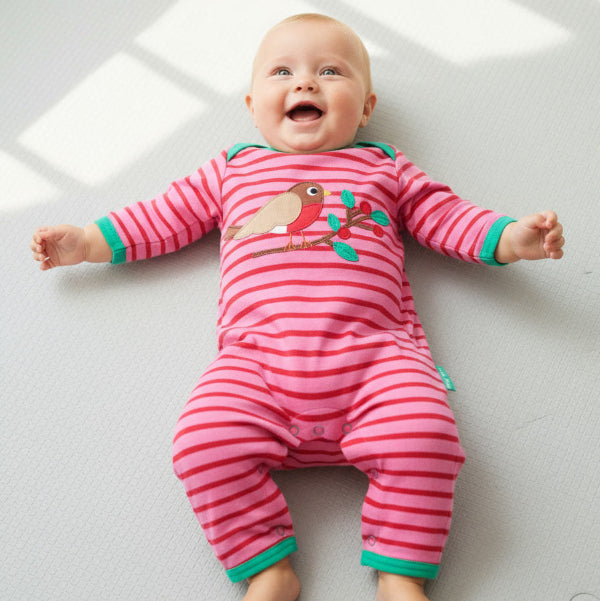 Baby wearing a pink striped onesie with a bird design on a light gray surface