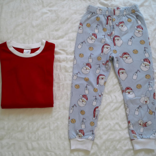 Red pajama top and blue pajama pants with Santa Claus pattern on a white bedspread.