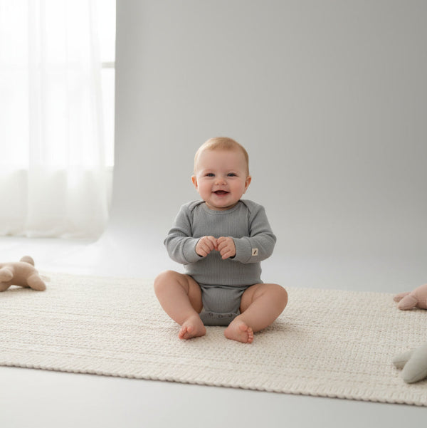 baby wearing grey turtle dow romper, sitting on a rug
