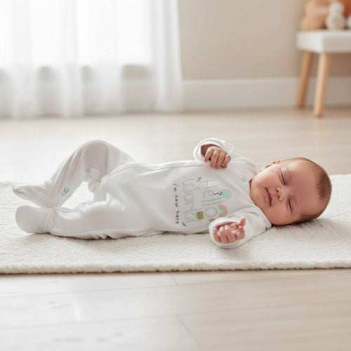 Newborn baby in a white onesie lying on a light-colored rug.