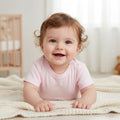 Baby in a pink shirt lying on a white blanket in a nursery