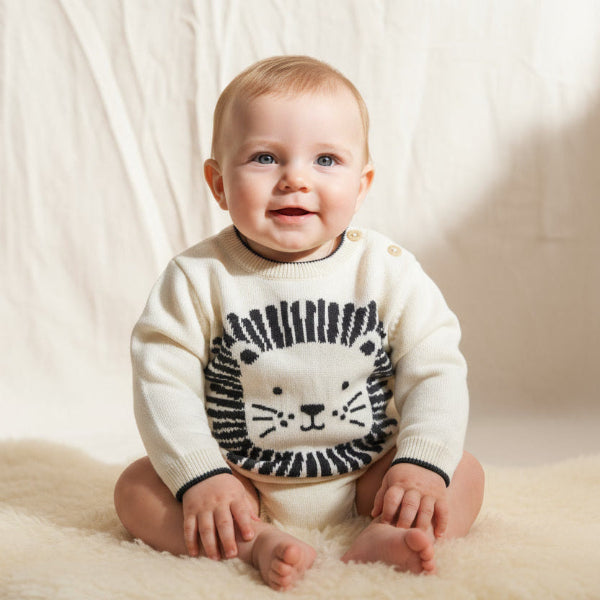 Baby wearing a white sweater with a lion design on a soft, light-colored background