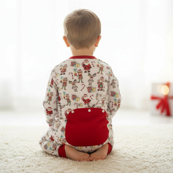 Child wearing a Christmas-themed onesie sitting on a carpeted floor with a blurred background of a decorated room.